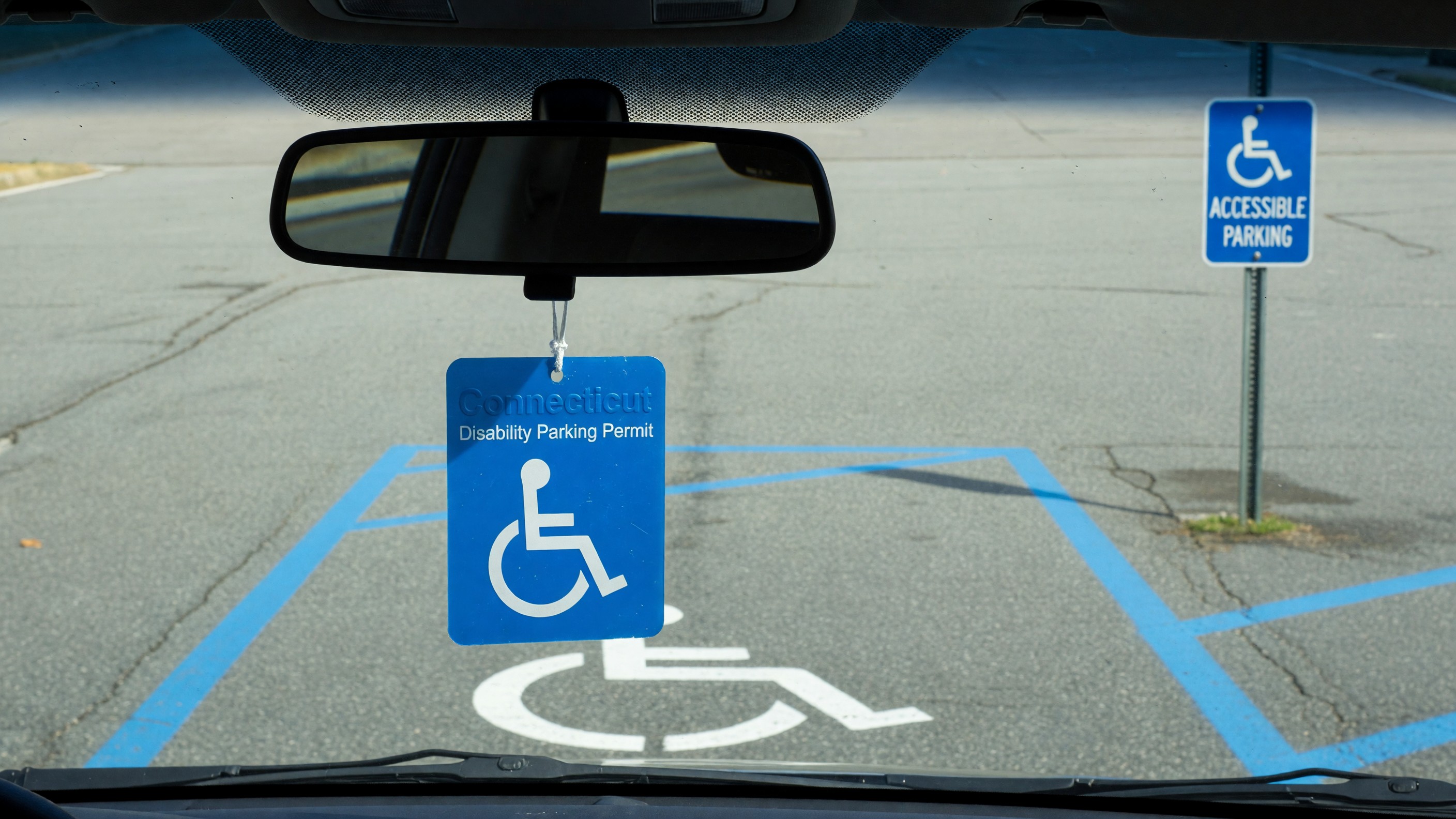 A Connecticut disability parking placard hanging from a vehicle rearview mirror in front of a designated accessible parking space.