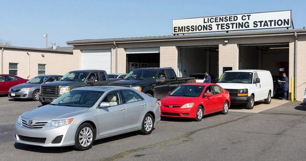 A row of vehicles queued at a licensed Connecticut emissions testing station on a clear day.