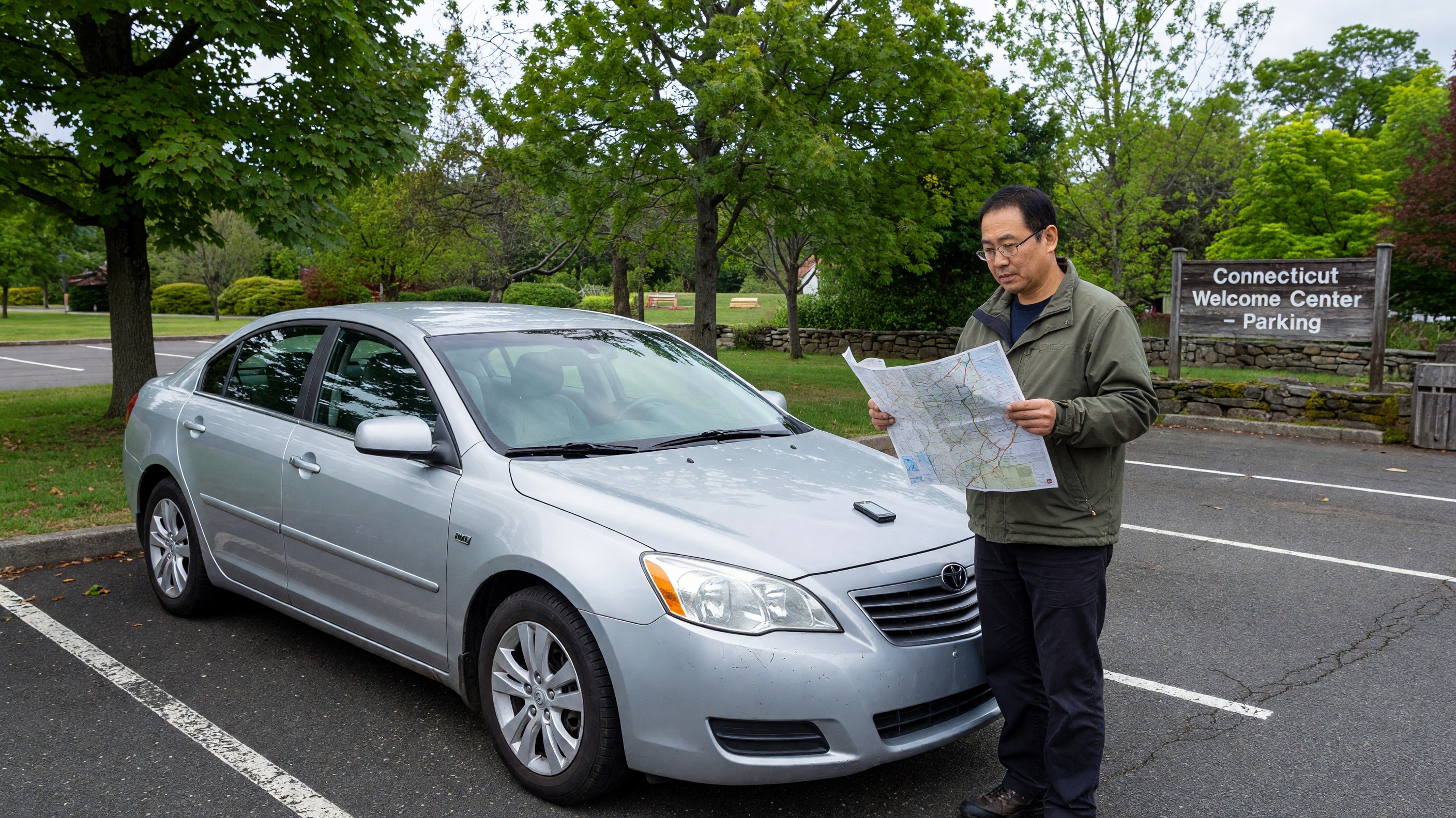 An international visitor reviewing directions beside a rental car in a Connecticut parking area.